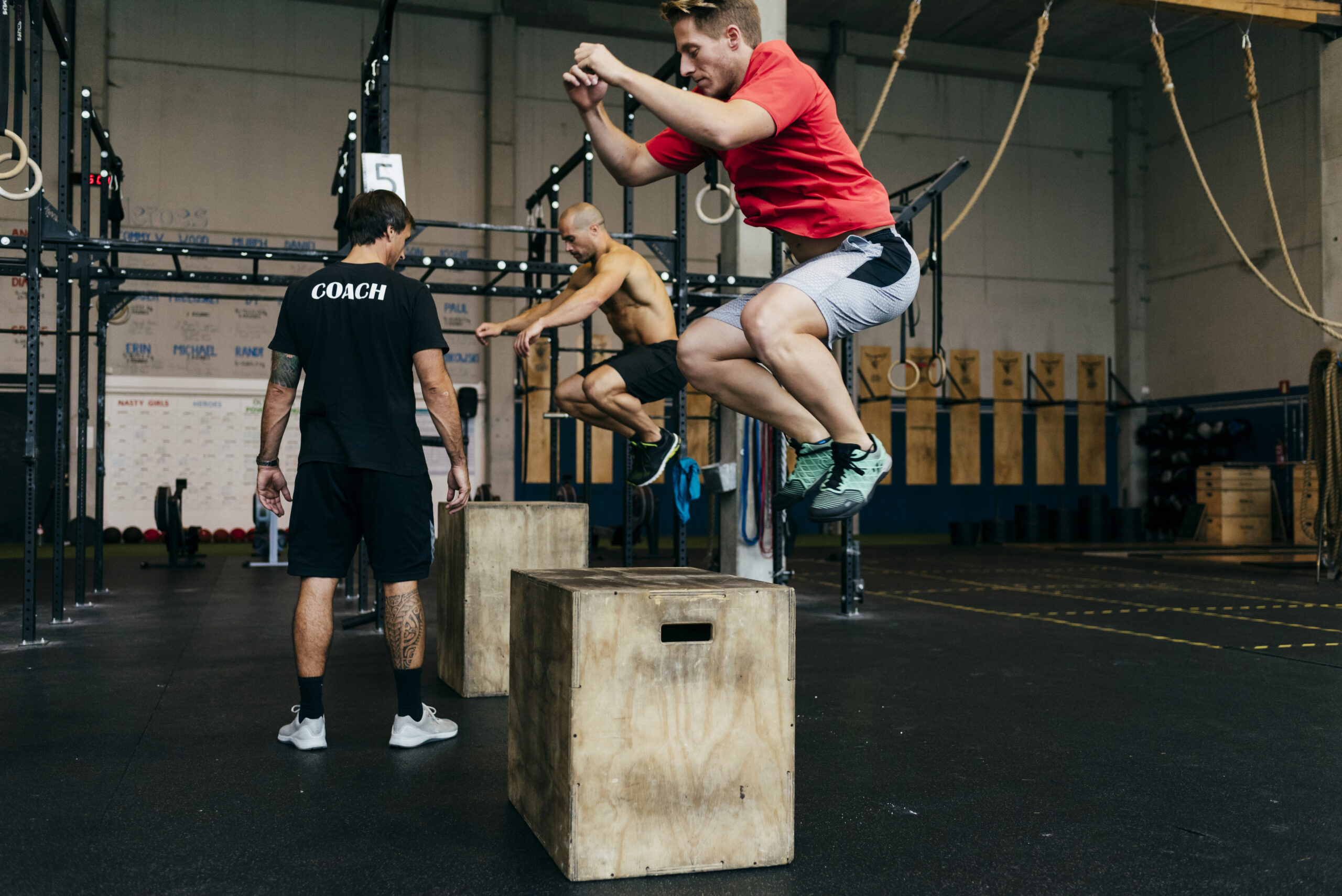 Sportsmen jumping on wooden cubes while training with coach in gym.