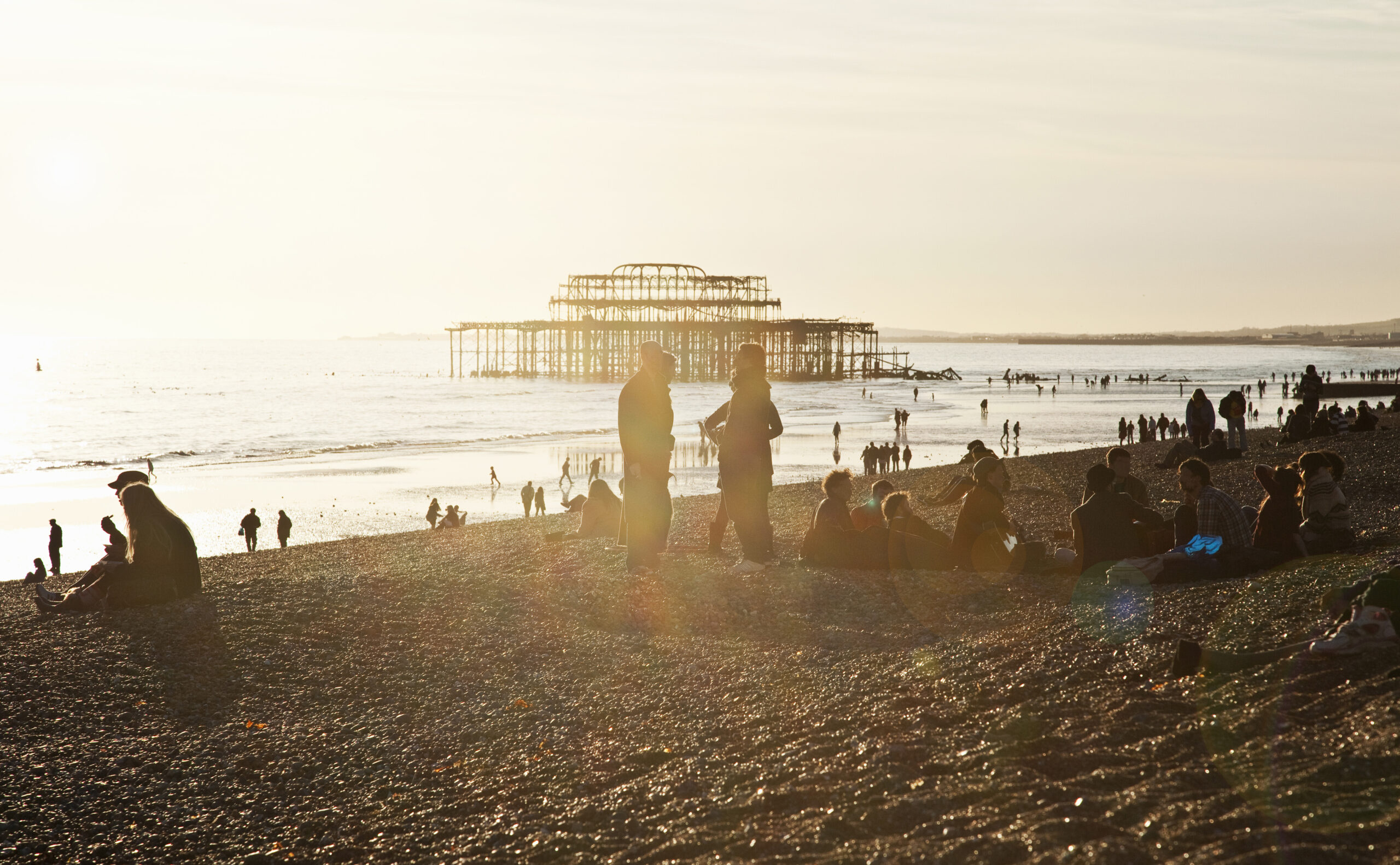 Silhouetted view of people on Brighton pier beach, Brighton, Sussex, UK