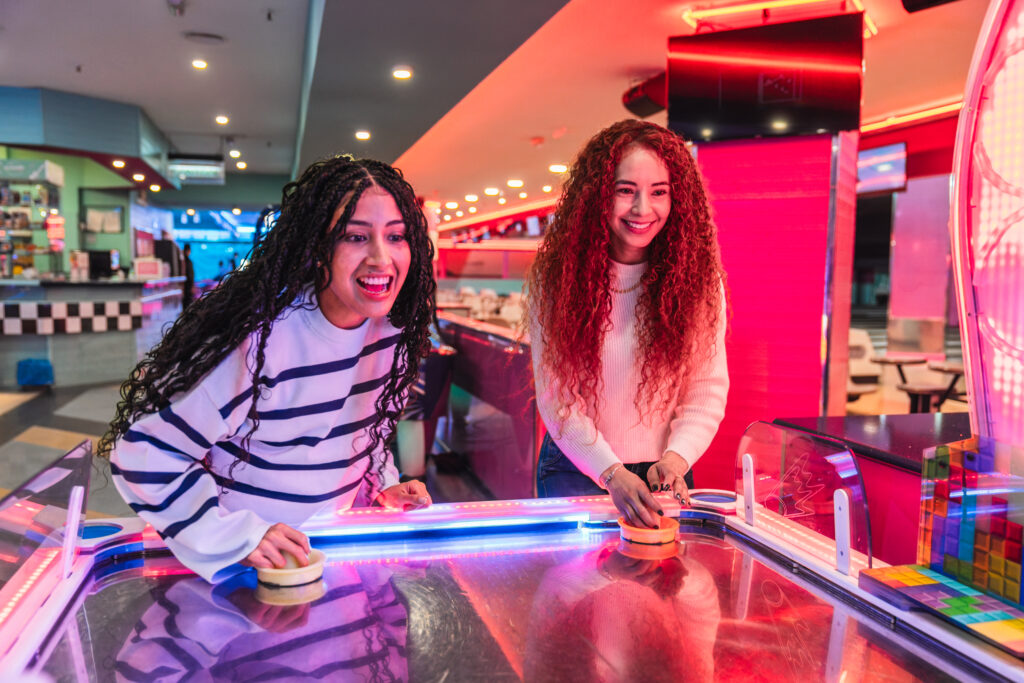 Two Friends Playing Air Hockey In Bowling Alley