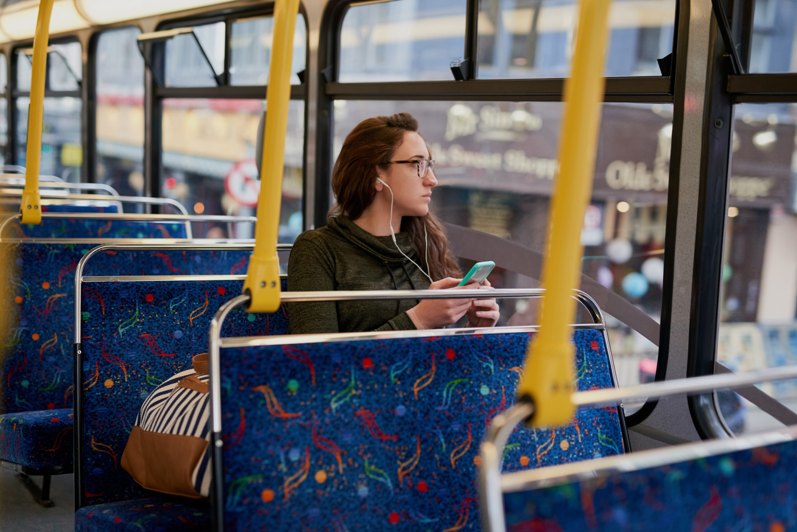 A woman sitting on a bus listening to music through headphones