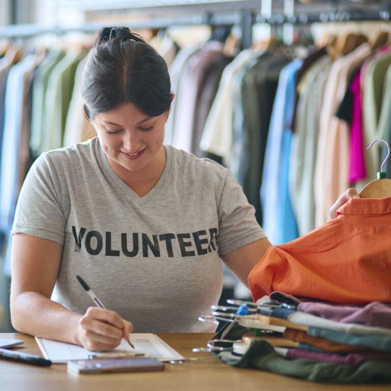 Volunteering in Brighton: Charity Worker At Desk With Clipboard Checking Clothing Donations At Thrift Store