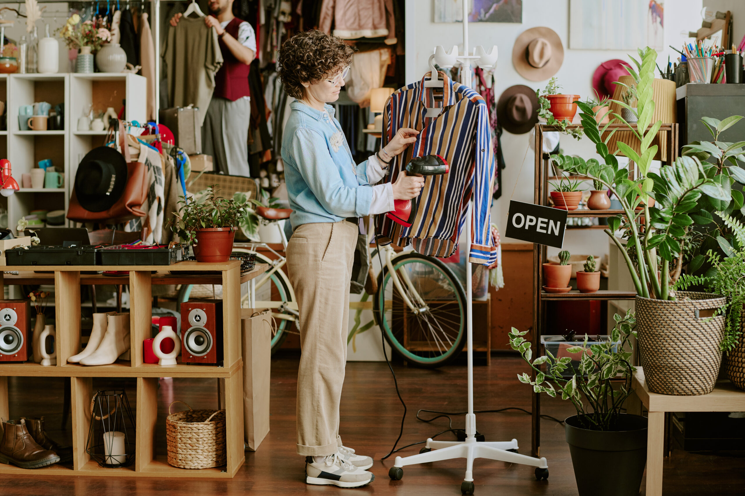 Woman organizing striped shirt display in chic boutique filled with various accessories.