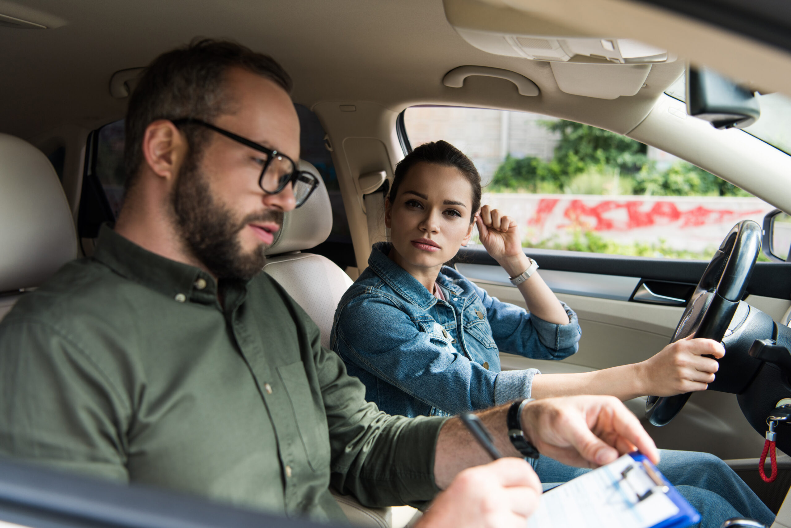 Woman Driving Car With Man Writing On Clipboard