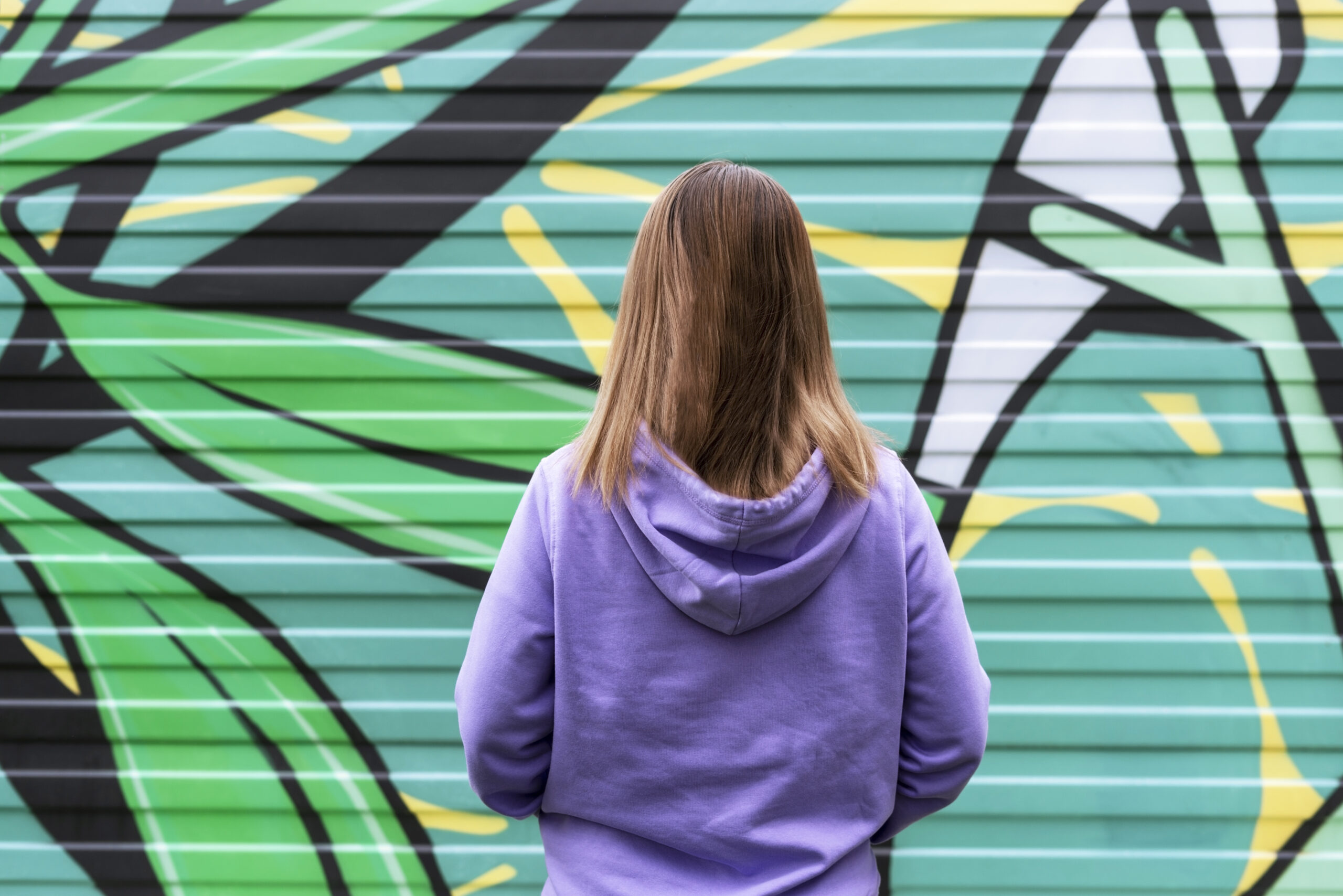 Young Blonde Woman In Purple Violet Hoodie staring at graffiti 