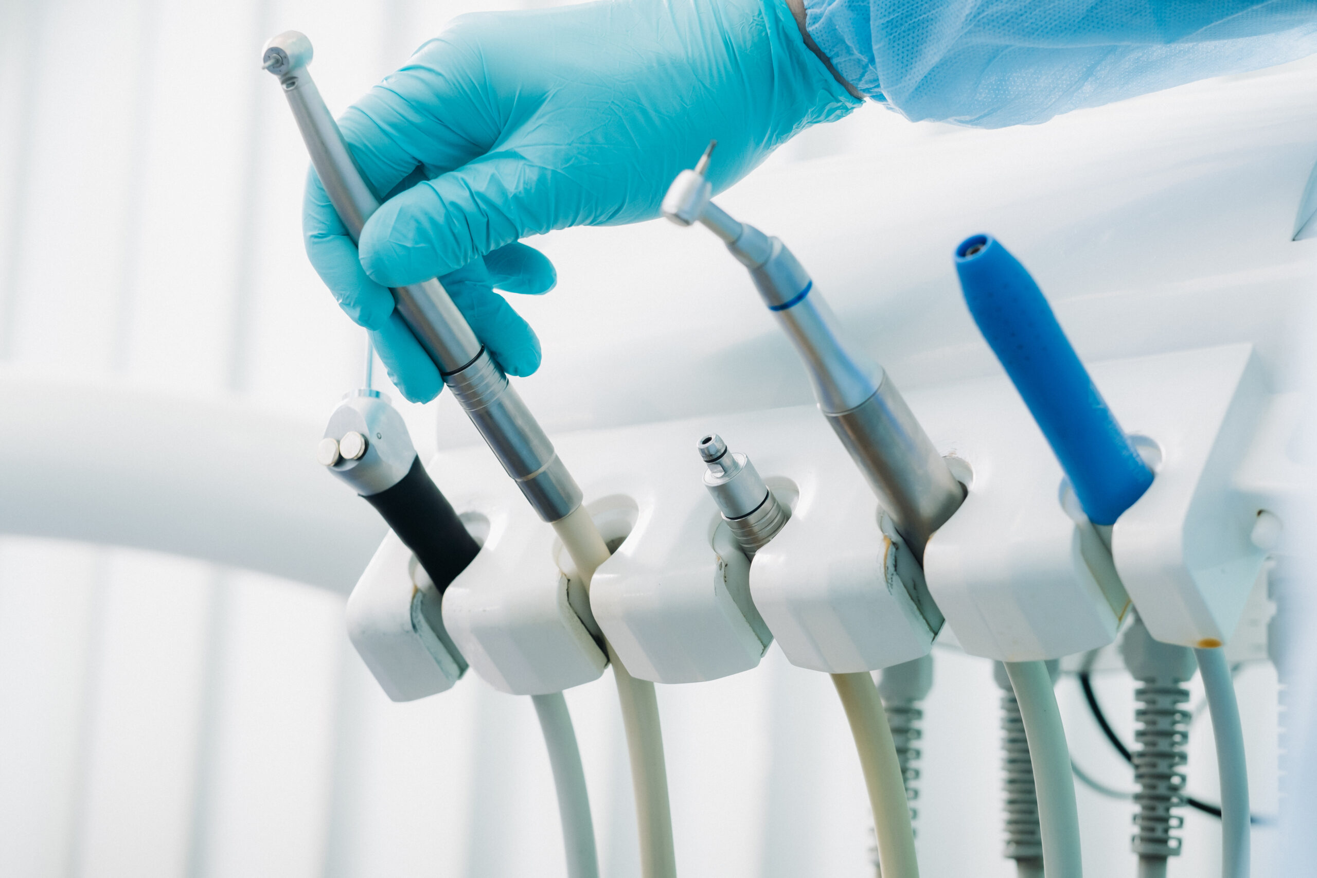 A dentist wearing gloves in the dental office holds a tool before working
