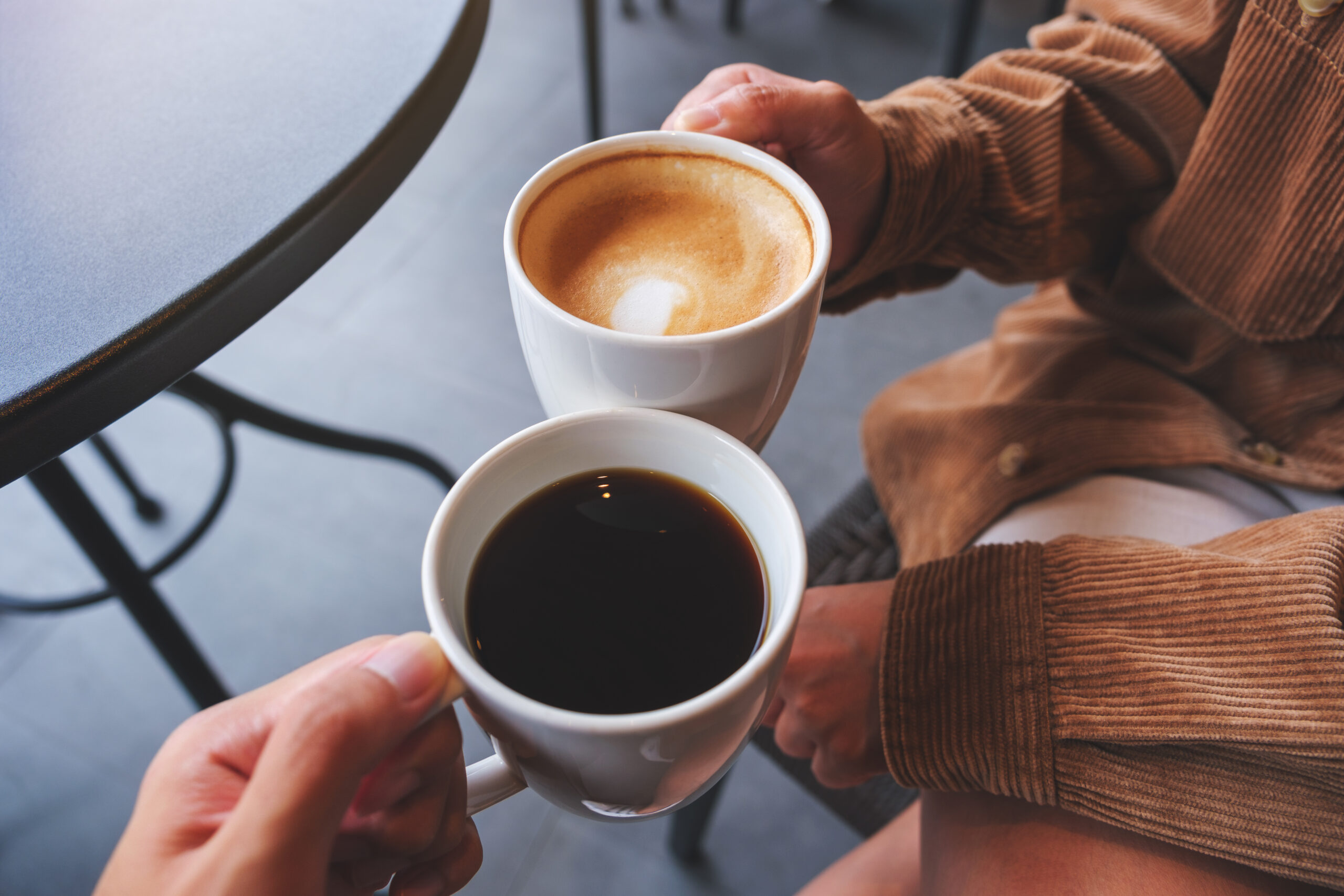 Closeup image of a couple people clinking white coffee mugs in café