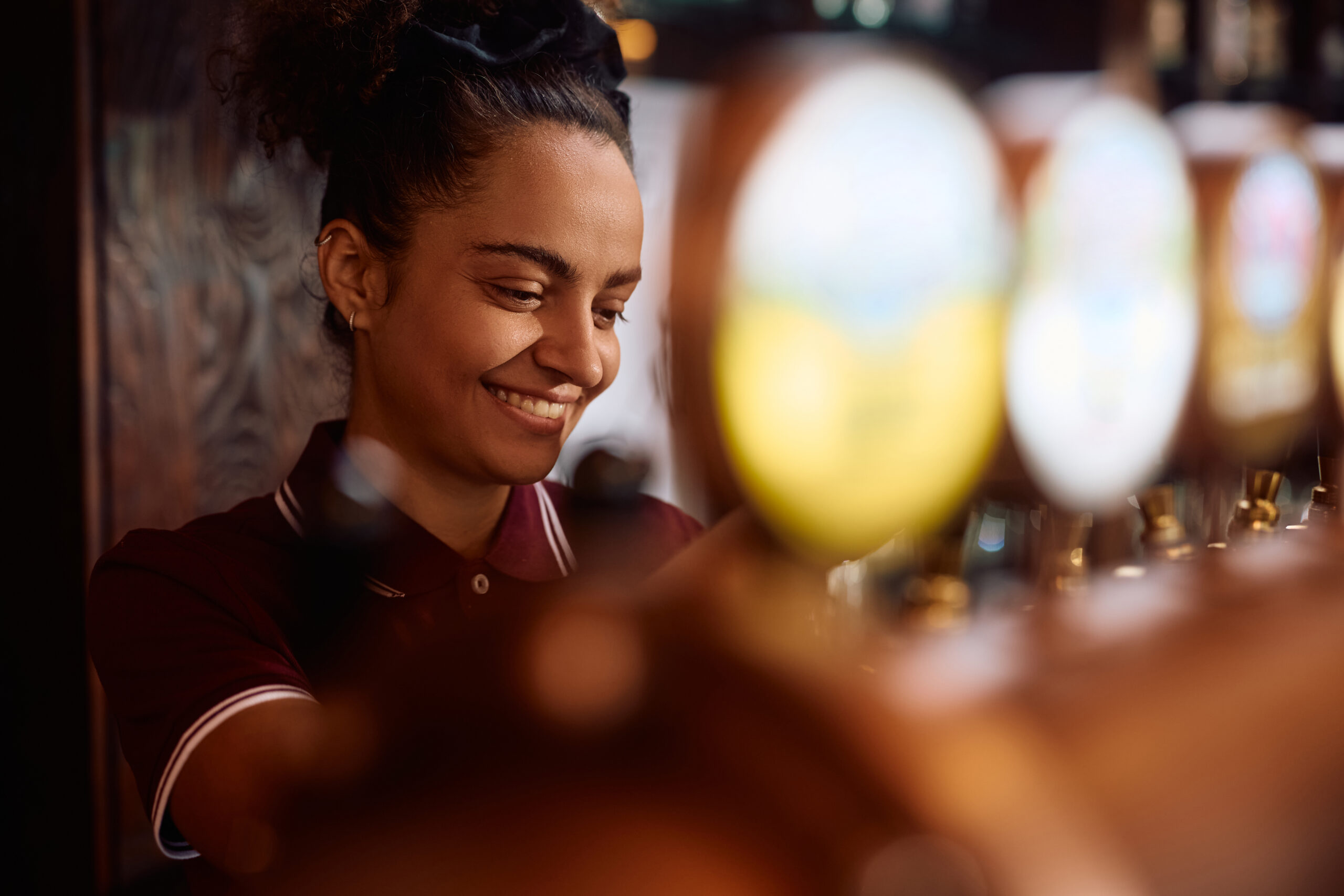 Young happy woman using beer tap while working as bartender in a pub.