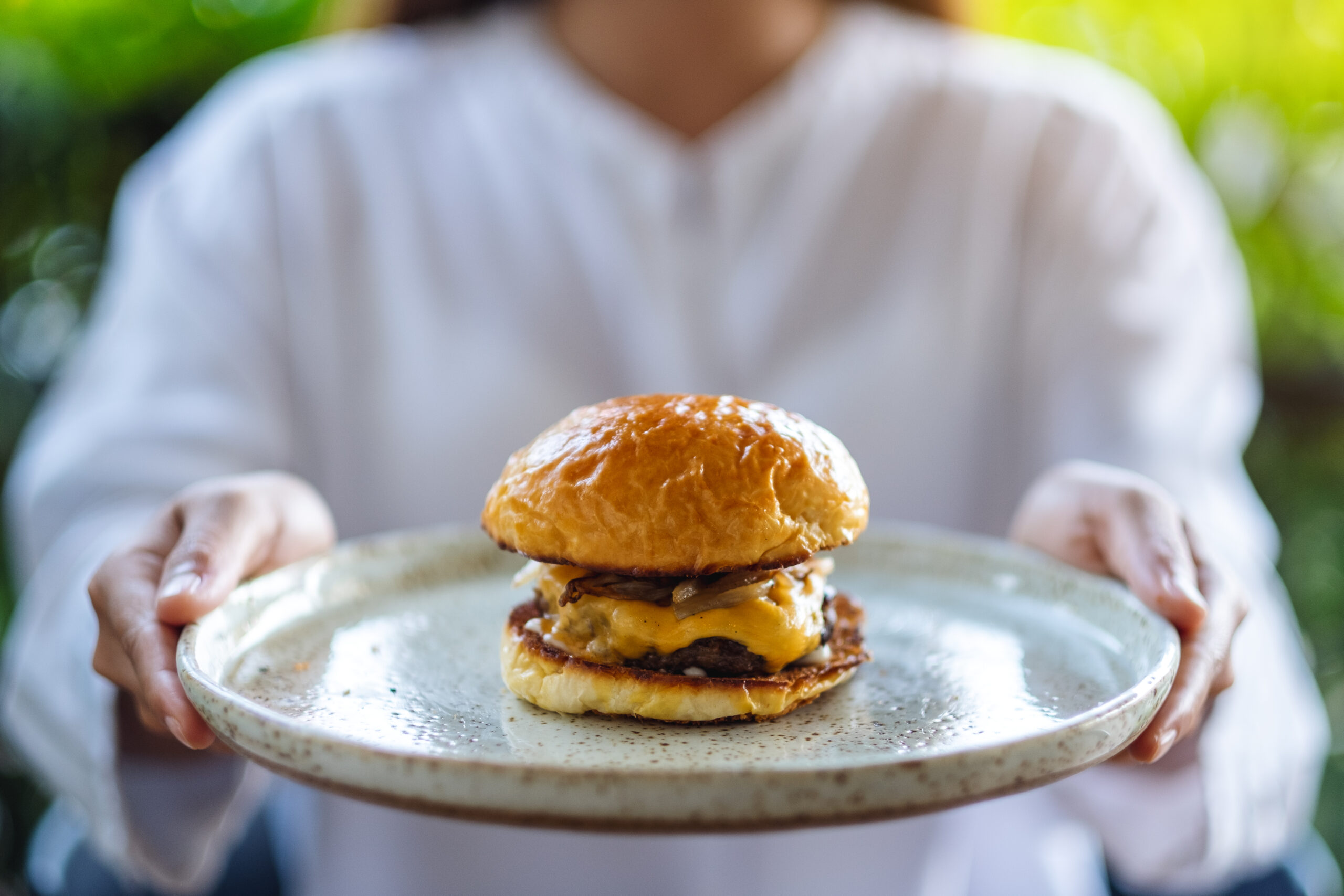 Closeup image of a woman holding and serving a plate of beef hamburger