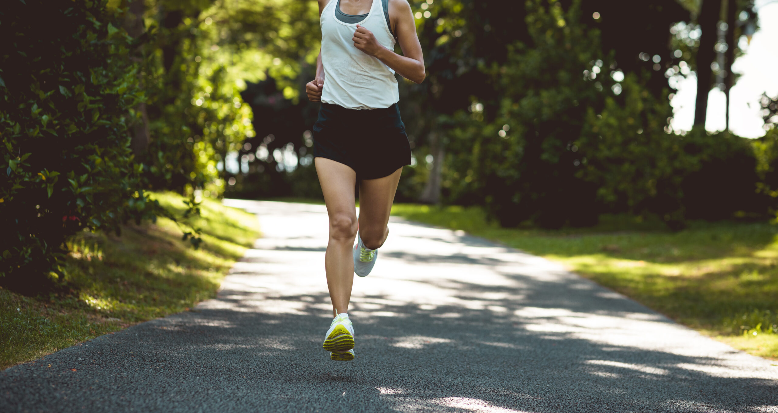 Fitness woman running on sunny  park trail