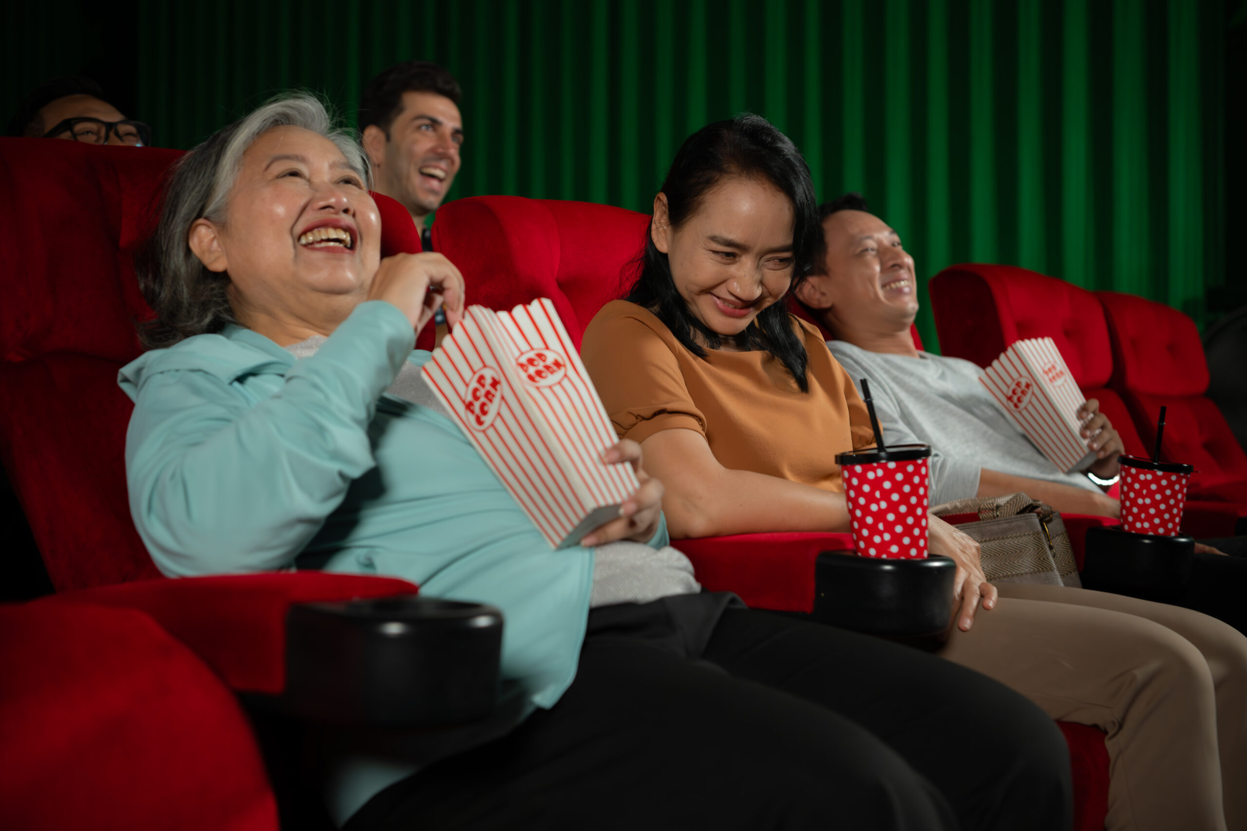 Group of adults watching a movie in a cinema and laughing with popcorn 