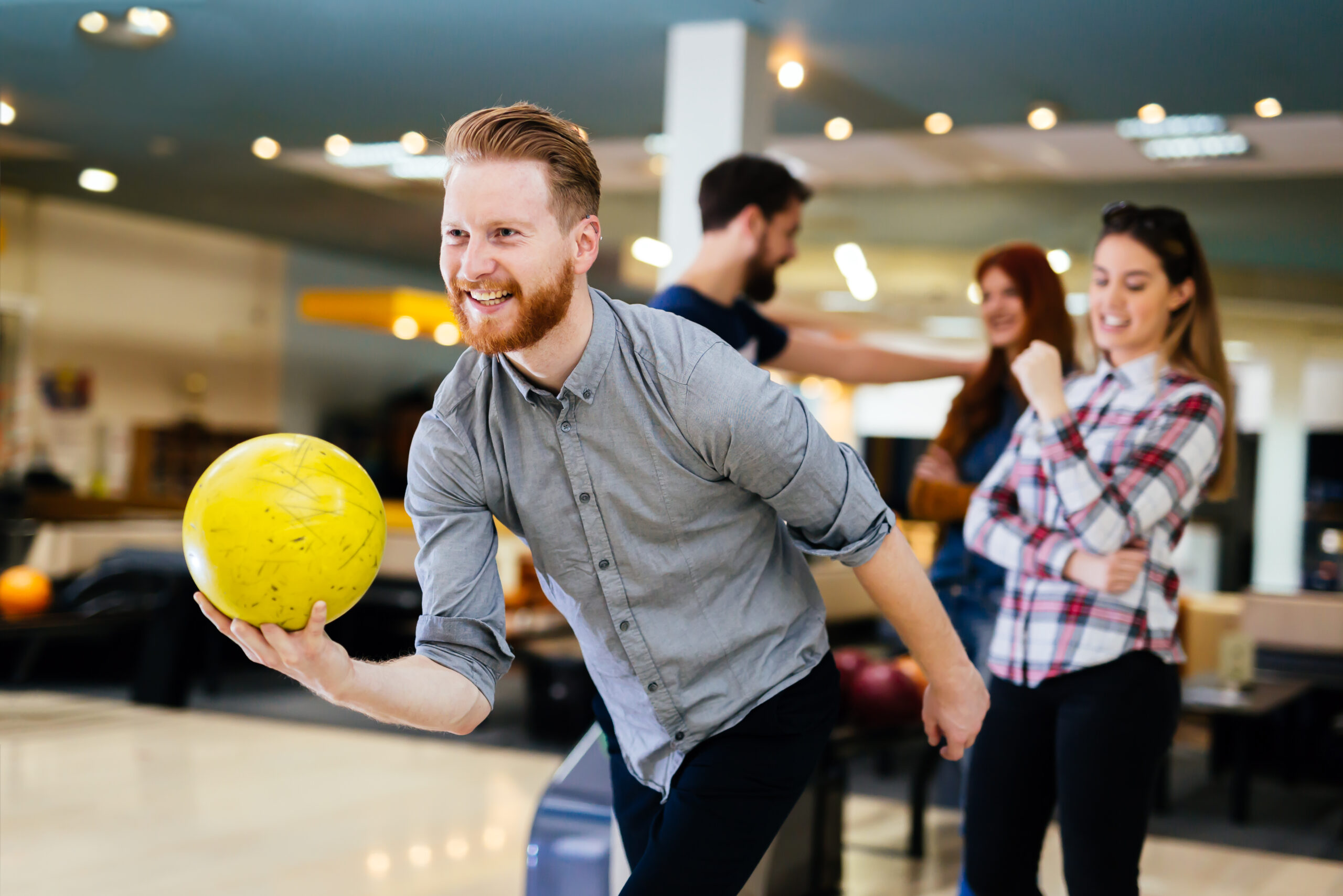 Smiling Man Bowling With Friends At Indoor Alley