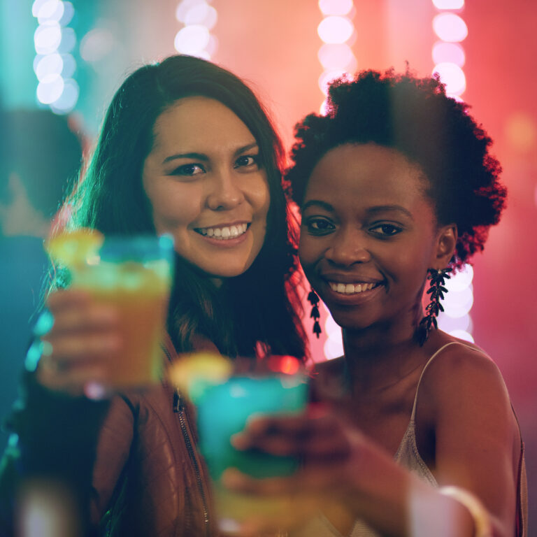 Two Smiling Women Toasting Colorful Cocktails