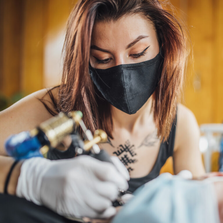 Woman Tattoo Artist Working Wearing Face Mask