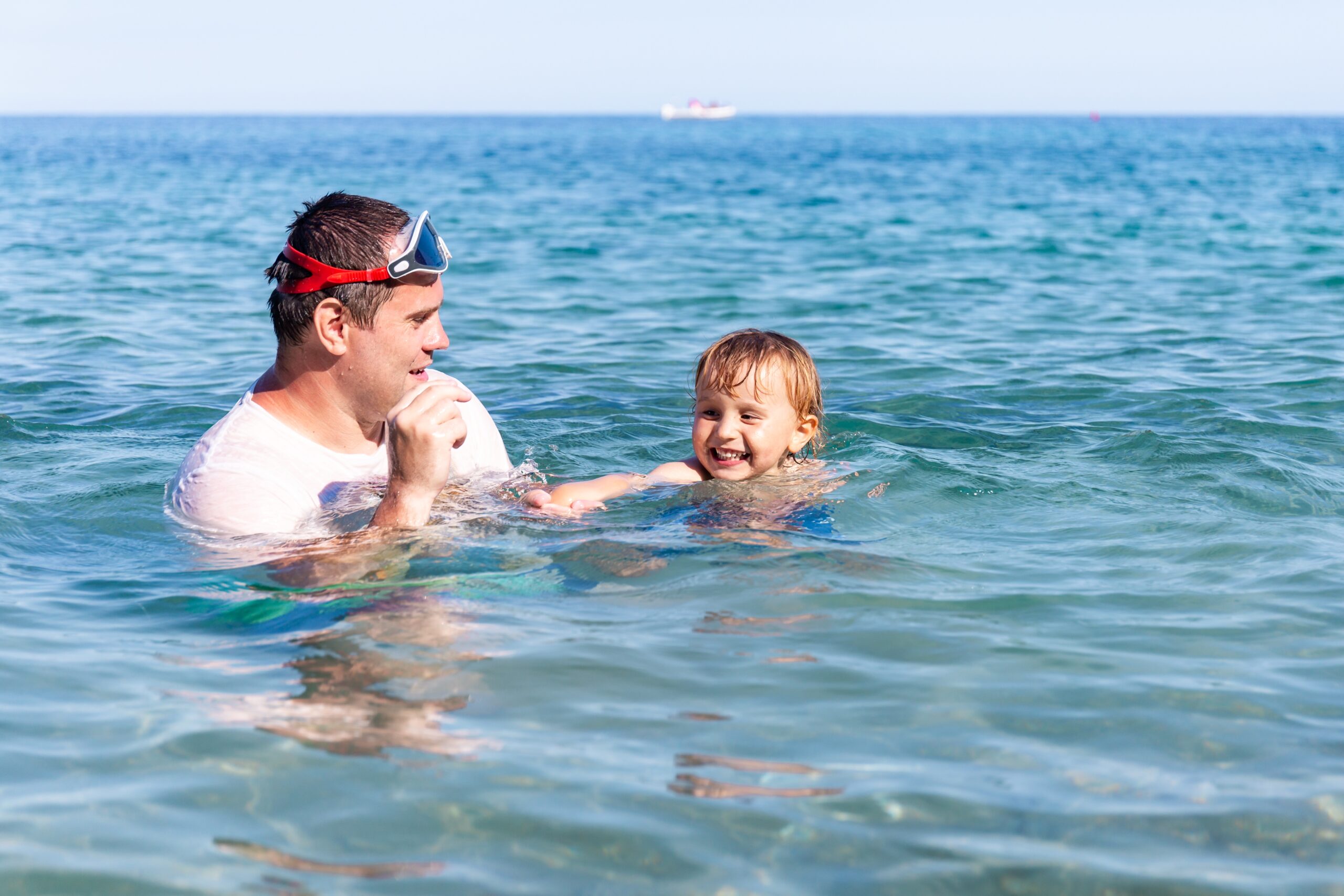 Father and little son having fun swimming and playing together in the sea.