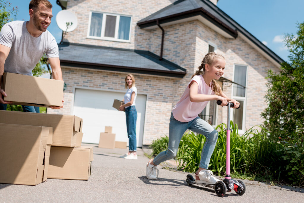 little kid riding on scooter with her parents unpacking cardboard boxes for relocation into new home