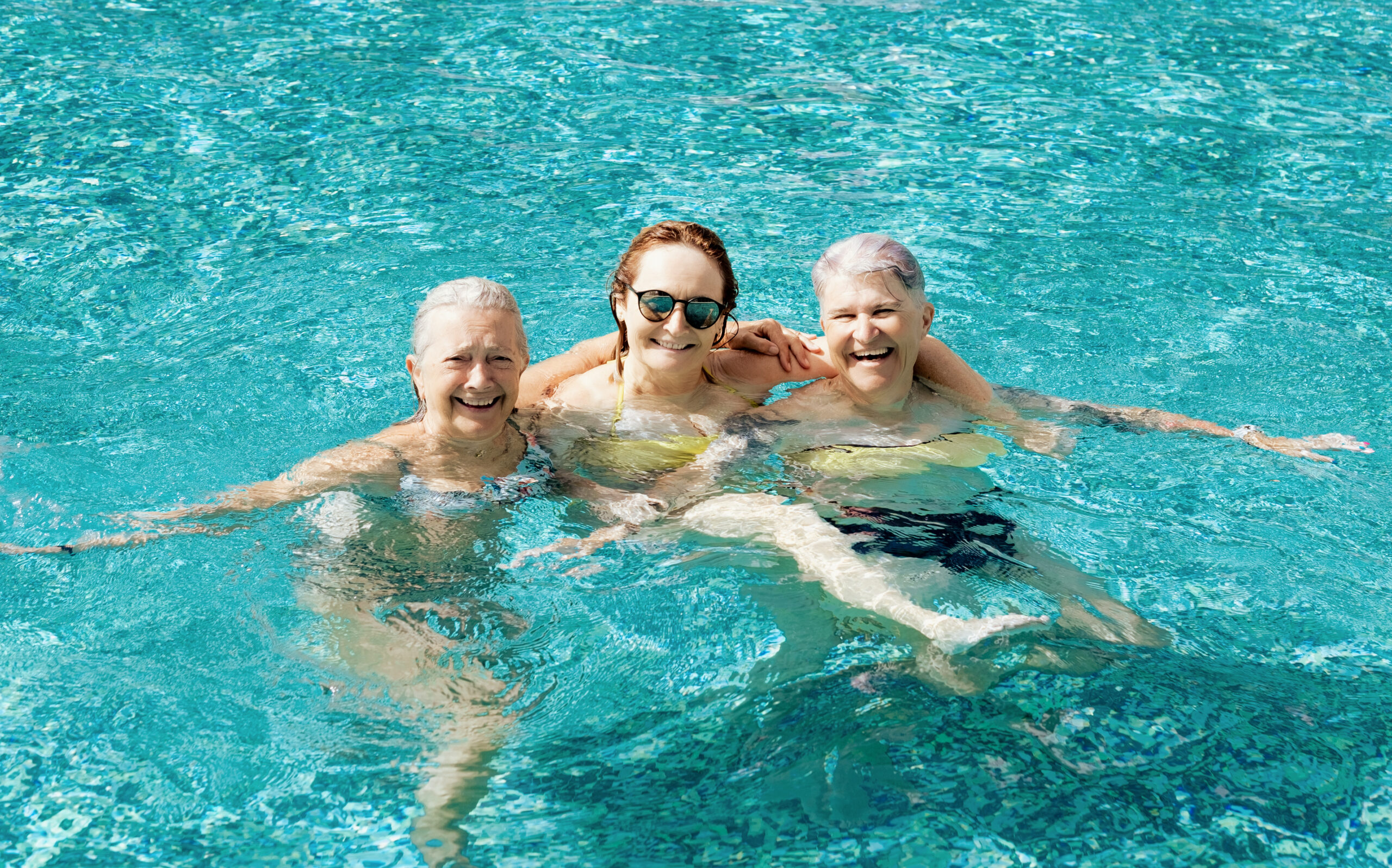 Three active mature senior women have fun in outdoor swimming pool under the sunlight