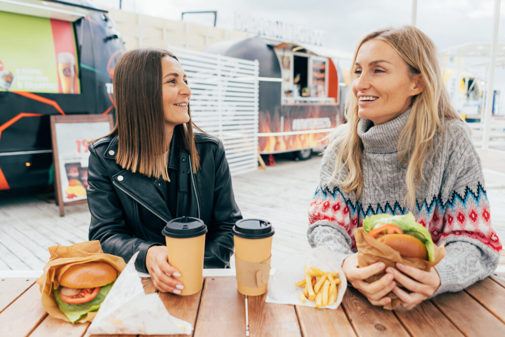Two girlfriends are chatting and eating fast food at the street market.