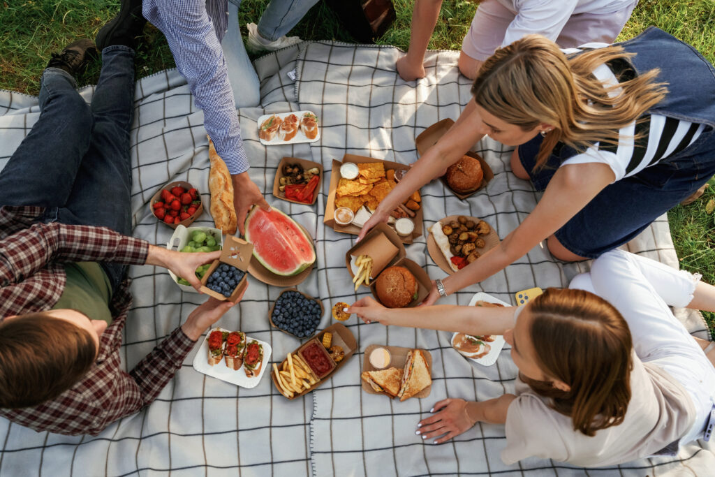 Group of friends are having picnic on the field with food in eco boxes.