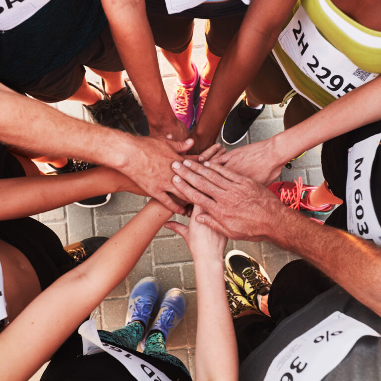 Hands of one of the run clubs in Brighton stacked on top of each other. Top view of a sports team standing in a circle with their hands stacked.