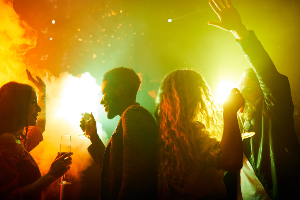 Happy excited young people dancing in smoke and drinking champagne while talking and enjoying party time
