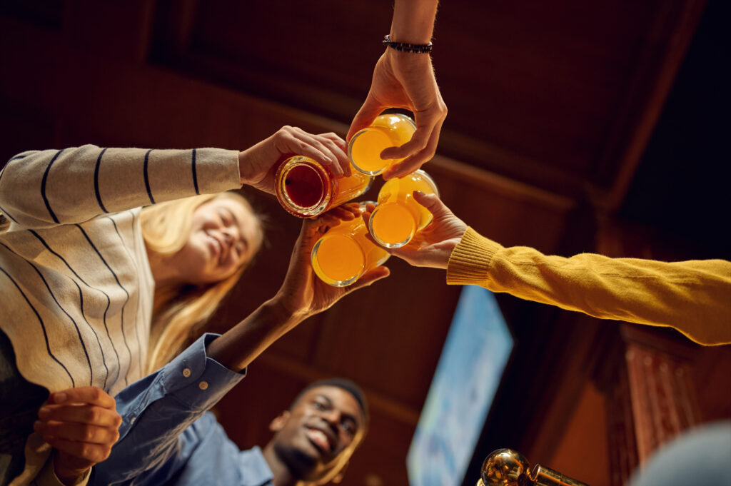Friends clink glasses with beer at the counter in bar.