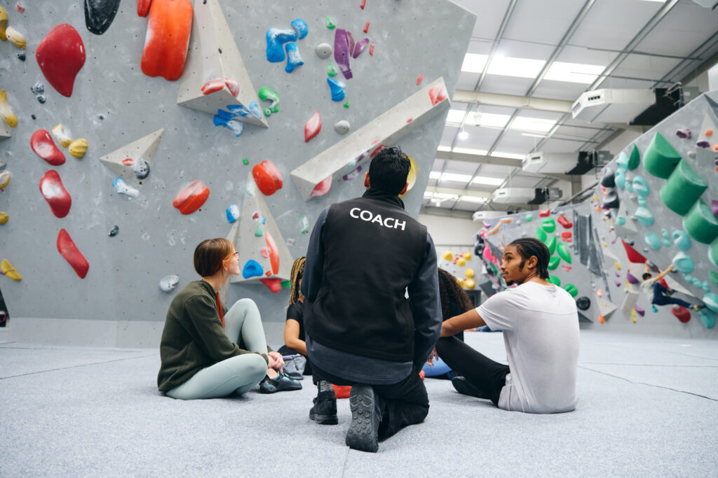Group of friends being given safety briefing by male coach at indoor wall climbing centre