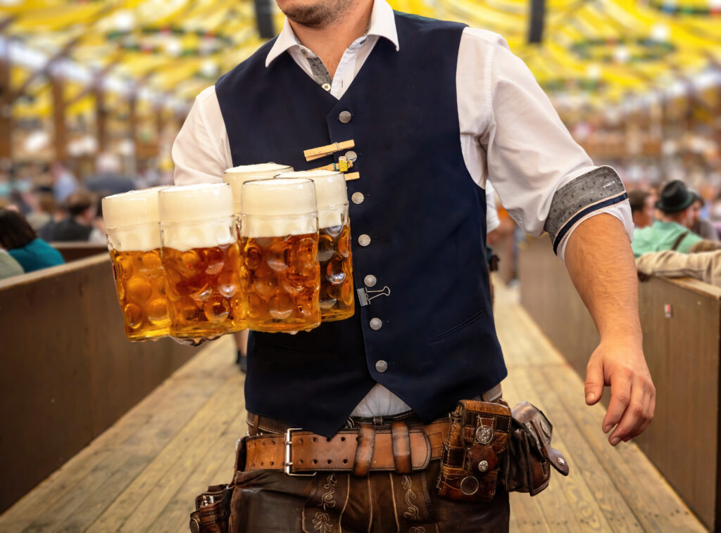 Waiter in traditional Bavarian costume serving beers, close up view.