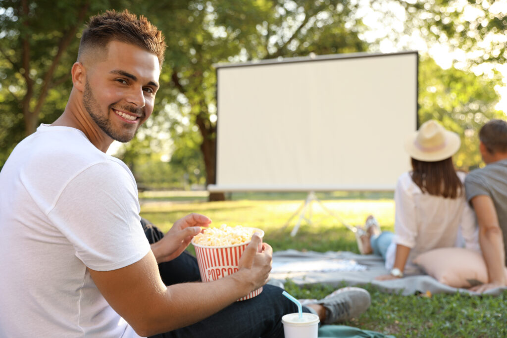 Young man with popcorn watching movie in open air cinema.